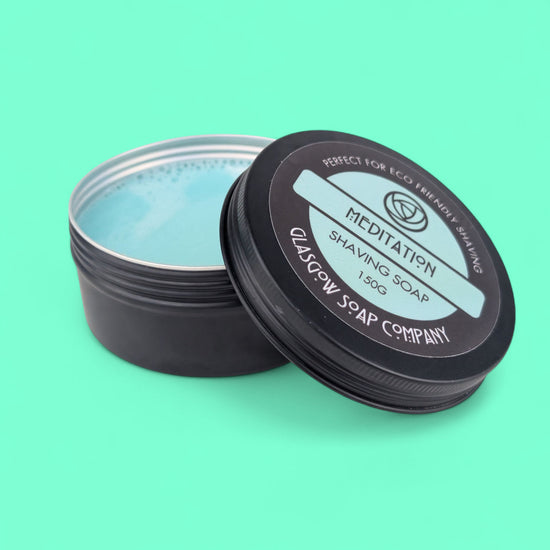 Black tin of shaving soap with 'Meditation' label on a teal background