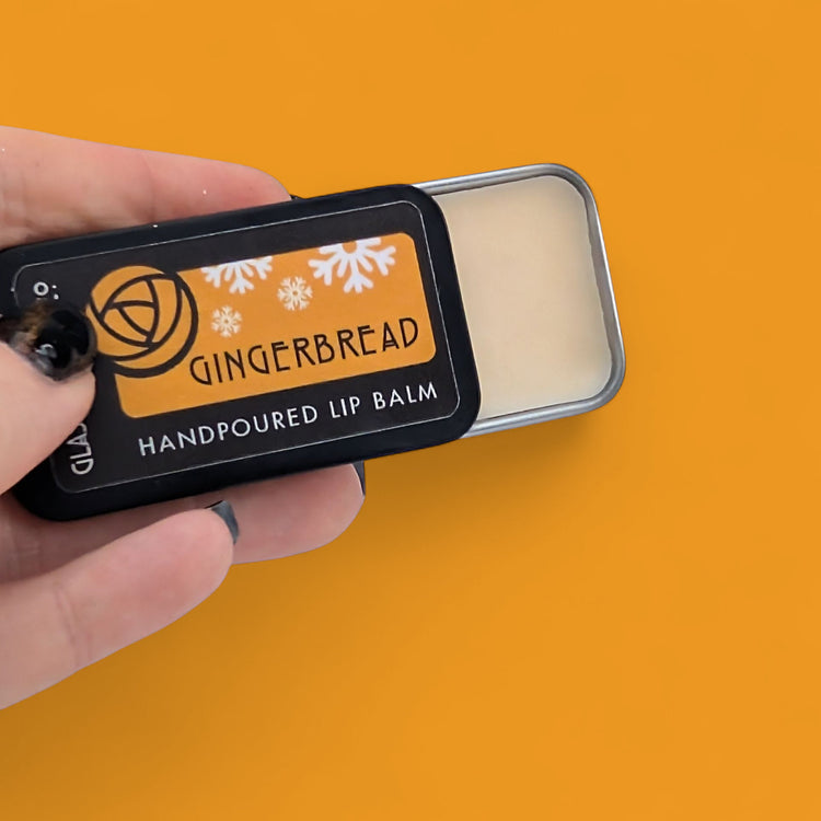 Hand holding a Gingerbread lip balm against an orange background