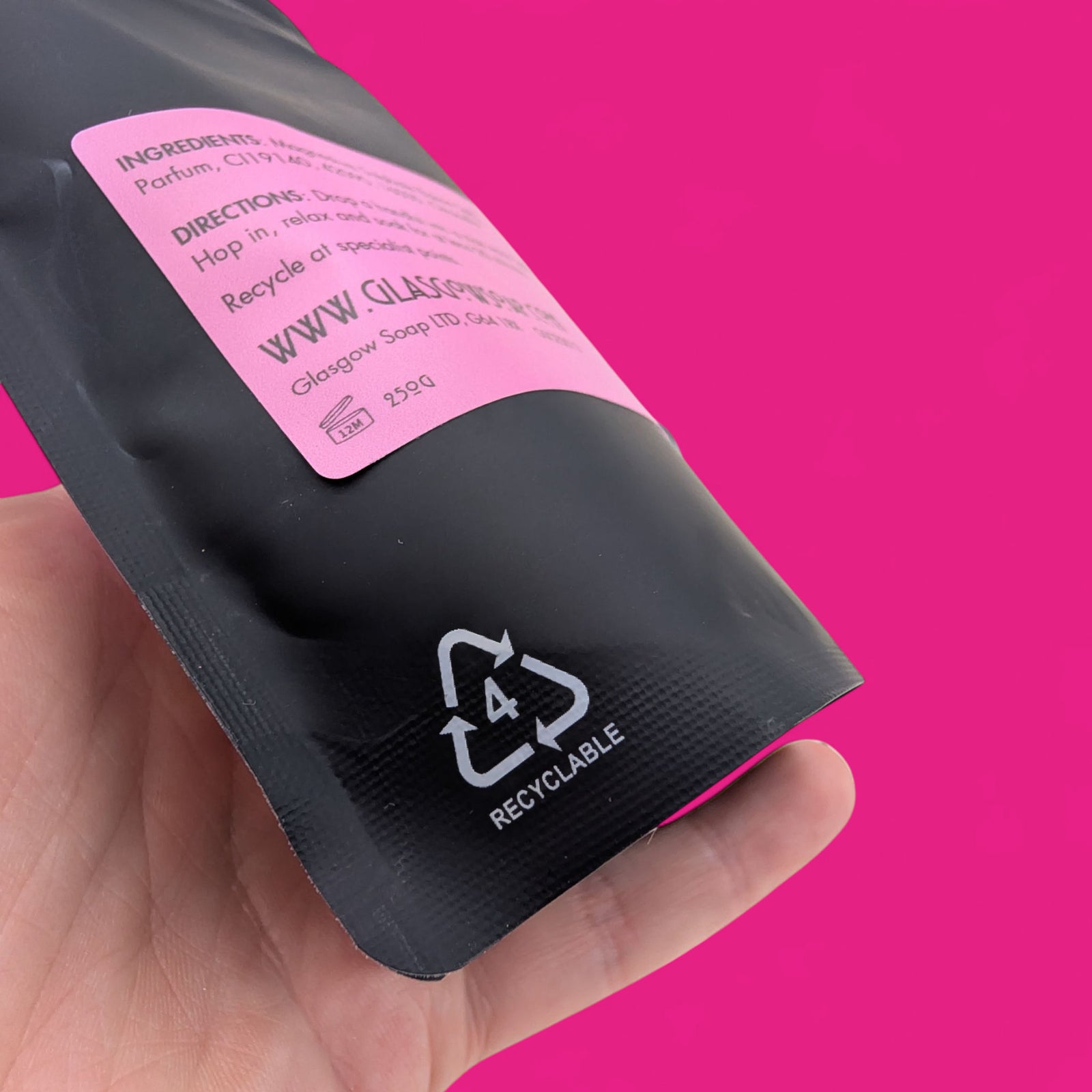 Hand holding a black and pink packaging with recycling symbol against a pink background