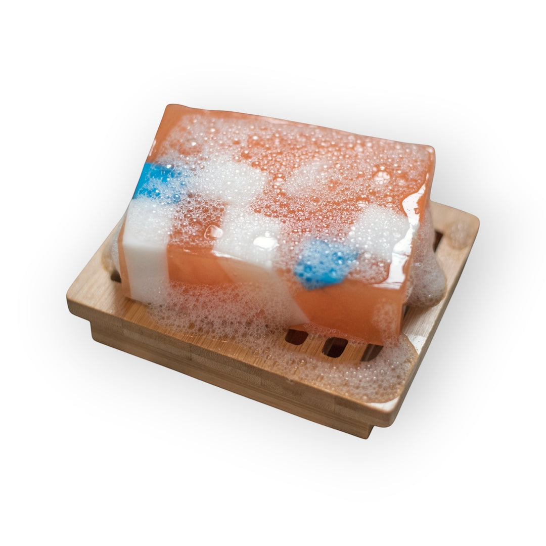 Glasgow Soap Company Ltd Iron Brew handmade soap bar with orange, white, and blue swirls on a bamboo soap dish with lather.
