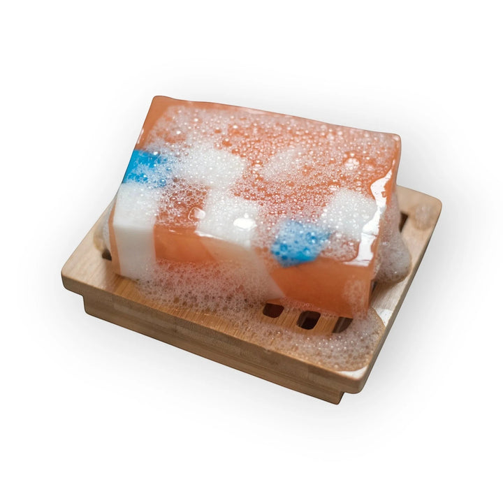 Glasgow Soap Company Ltd Iron Brew soap bar with orange, white, and blue swirls, on a bamboo soap dish with lather.