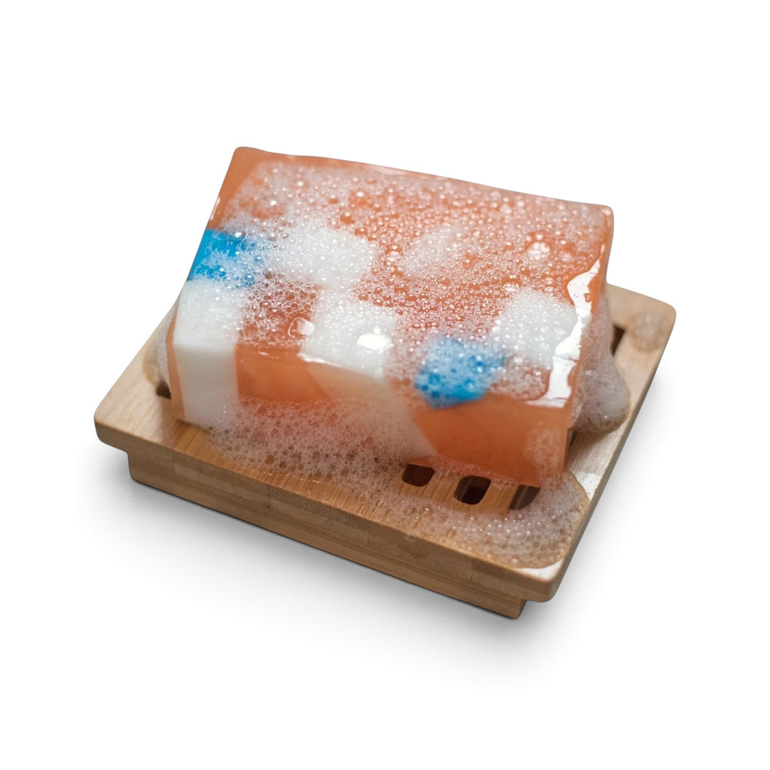 Glasgow Soap Company Ltd Iron Brew soap bar with orange, white, and blue cubes on a wooden soap dish with lather.