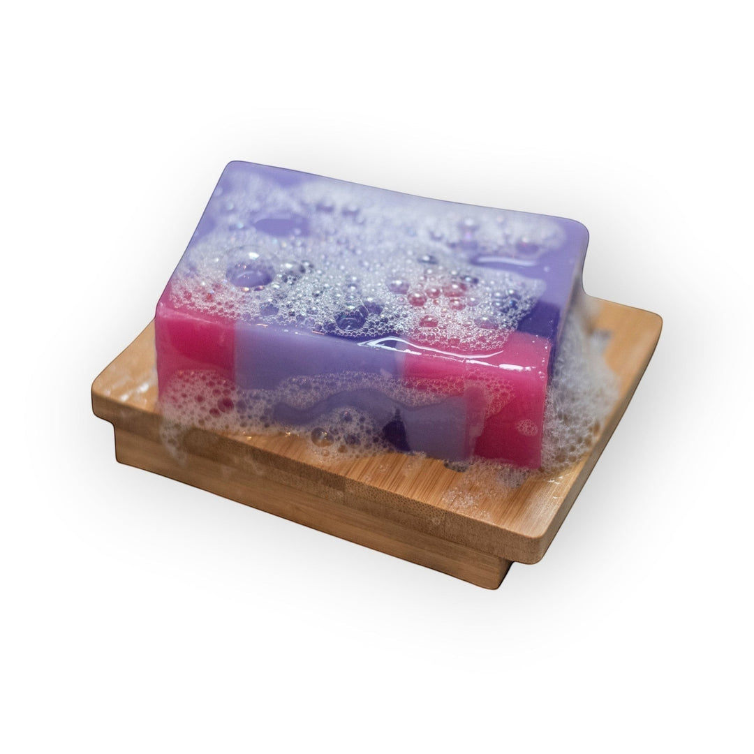 Glasgow Soap Company Ltd Parma Violet soap slice with pink and purple layers, on a bamboo soap dish with bubbles.