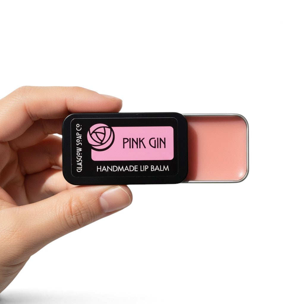 Glasgow Soap Company Ltd Pink Gin lip balm in a sliding black tin held in a hand, featuring a raspberry flavour.