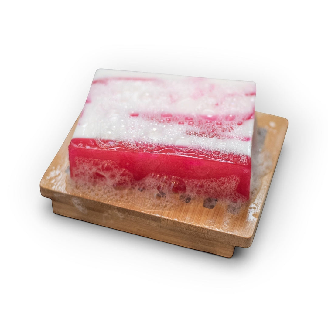 Glasgow Soap Company Ltd Raspberry Ripple soap bar with pink and white swirls on a wooden soap dish with soap bubbles