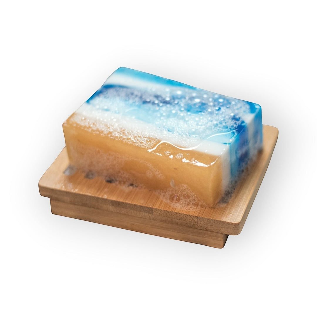 Glasgow Soap Company Ltd sea salt and driftwood bar soap with blue ocean waves and sandy beach design, on a wooden soap dish.
