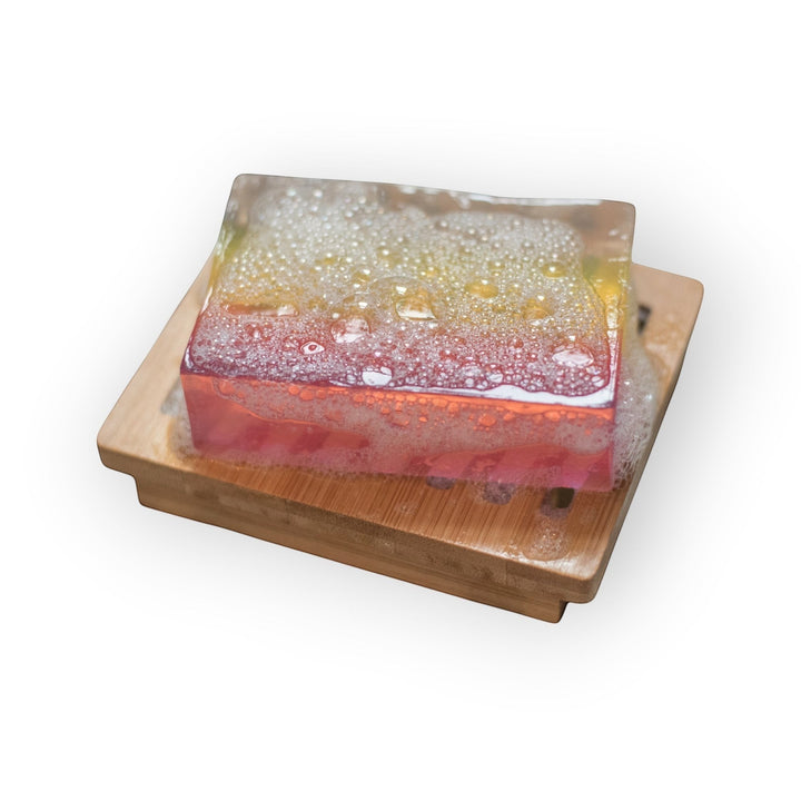 Glasgow Soap Company Ltd rhubarb and ginger soap slice with pink and yellow layers, on a bamboo soap dish with lather.