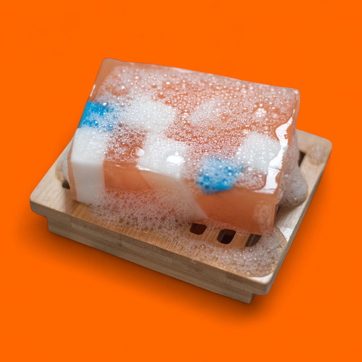 Bar of soap with bubbles on a wooden soap dish against an orange background