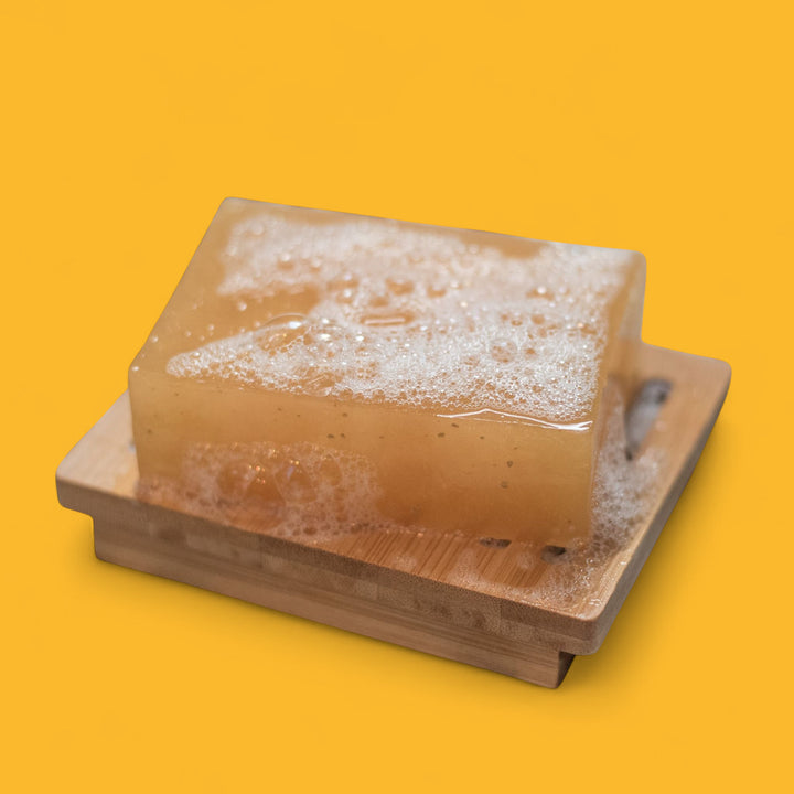 Bar of soap with suds on a wooden soap dish against a yellow background