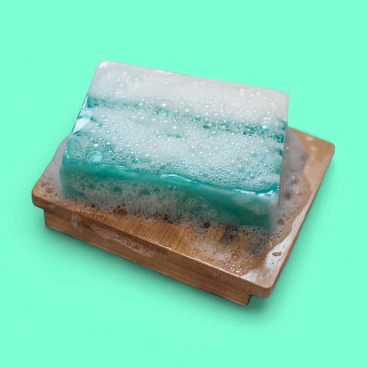 Foamy bar of soap on a wooden soap dish against a green background