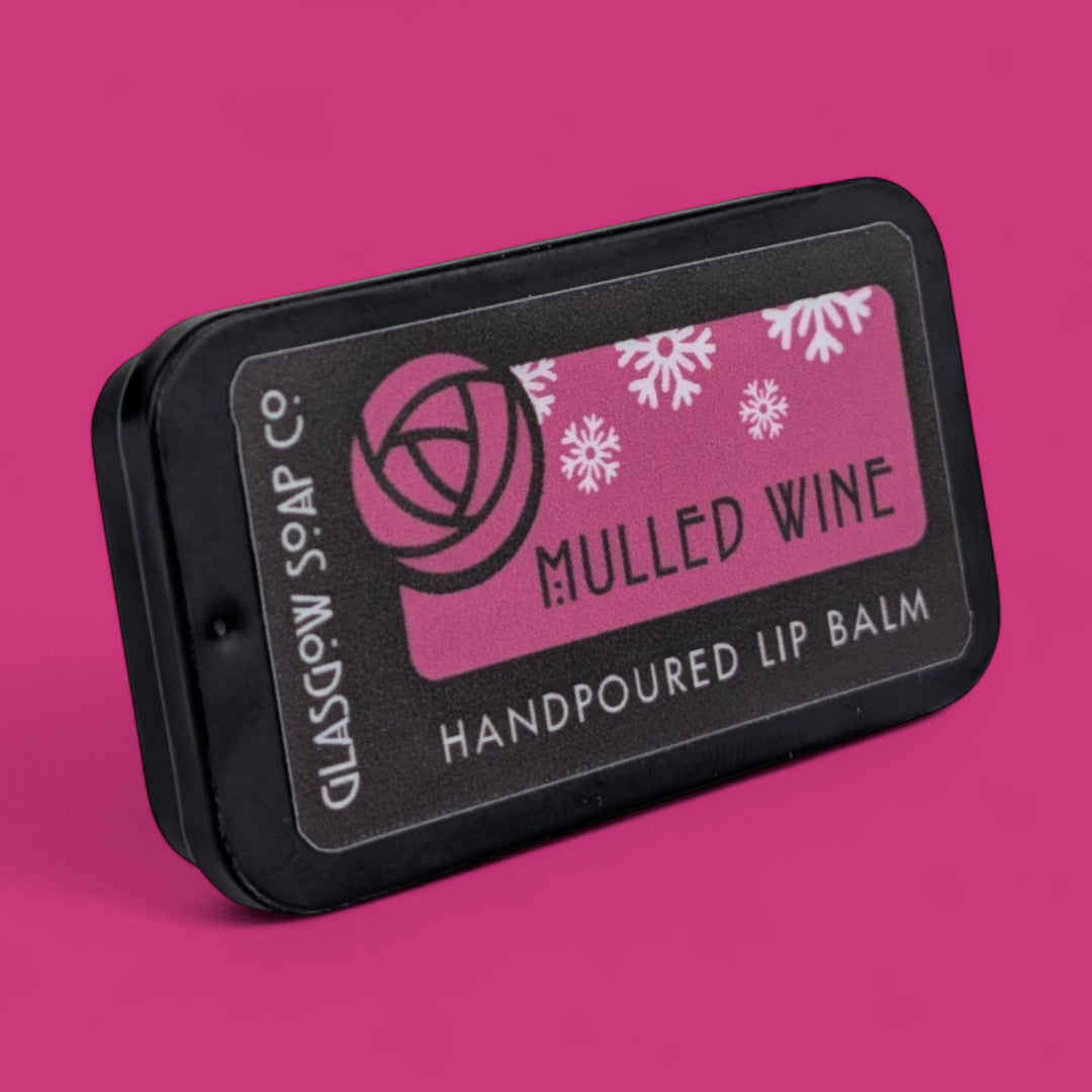 Handpoured lip balm tin labeled 'Mulled Wine' with Glasgow Soap Co branding on a pink background.
