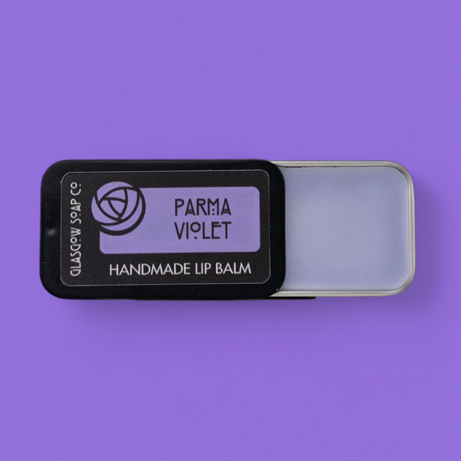 Handmade lip balm in a black tin labeled 'Parma Violet' on a purple background
