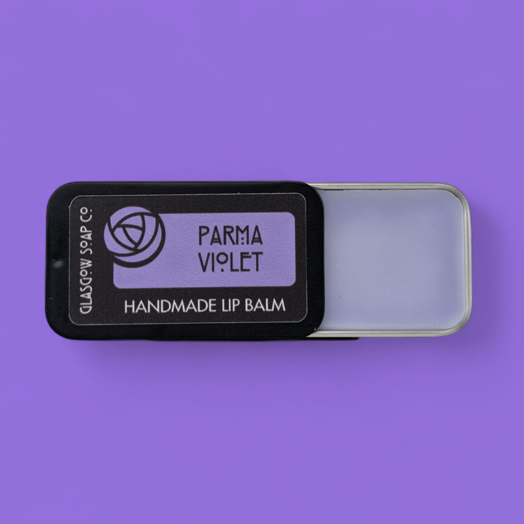 Handmade lip balm in a black tin labeled 'Parma Violet' on a purple background