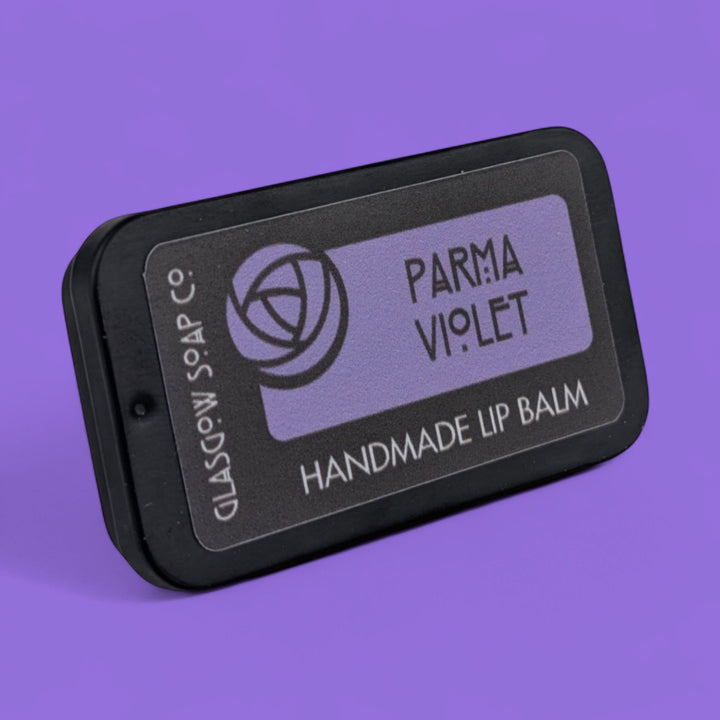 Handmade lip balm with 'Parma Violet' scent on a purple background