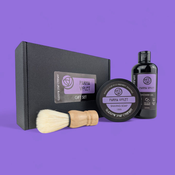 Parma Violet grooming set with black box, brush, vegan soap, and shower gel on a purple background