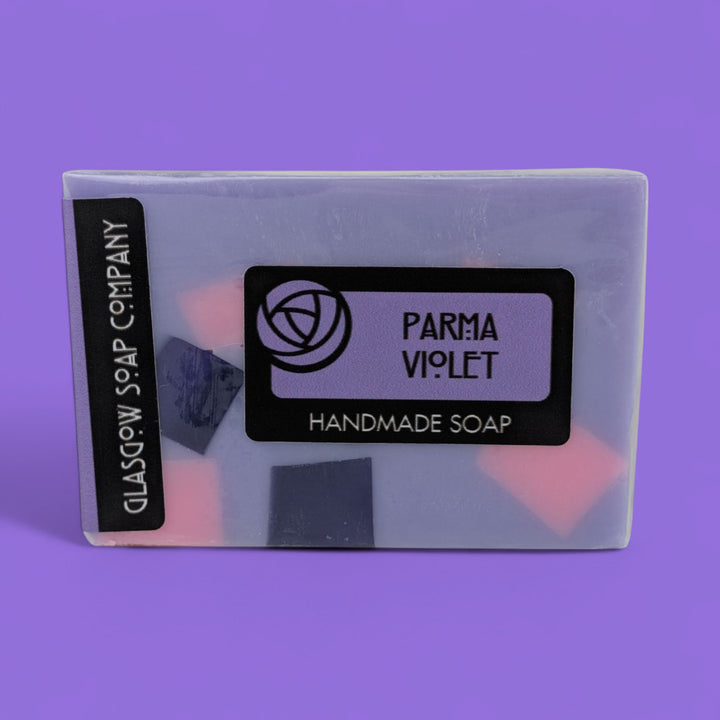 Handmade soap bar with 'Parma Violet' fragrance on a purple background
