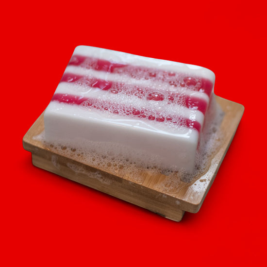 Bar of soap with red and white stripes on a wooden soap dish against a red background