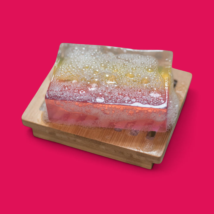 Colorful layered soap on a wooden tray with a pink background