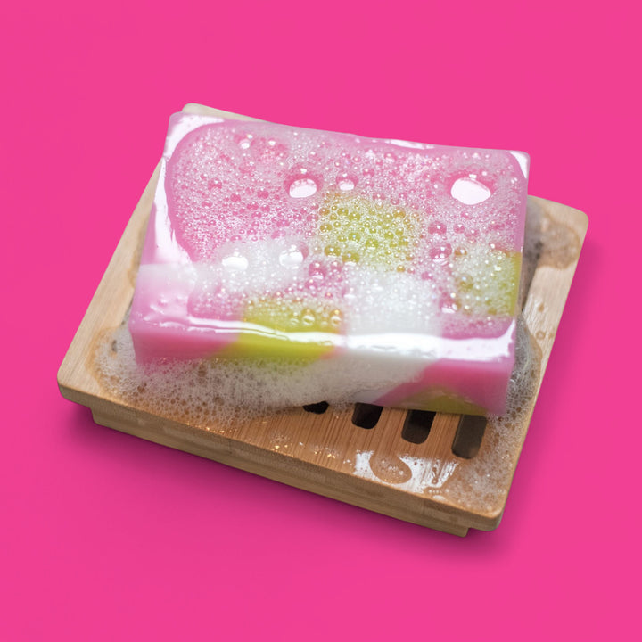 Colorful soap bar with bubbles on a wooden soap dish against a pink background