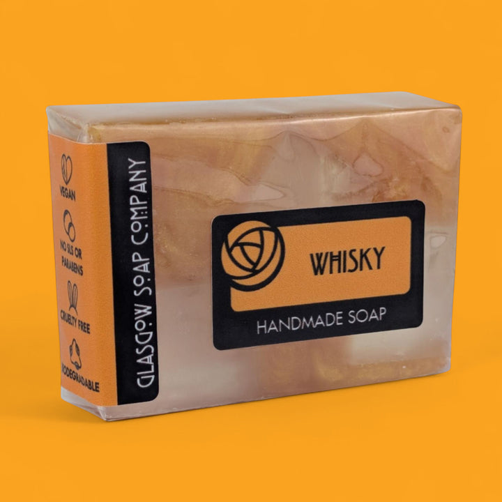 Handmade soap bar with 'Whisky' flavor packaging on an orange background