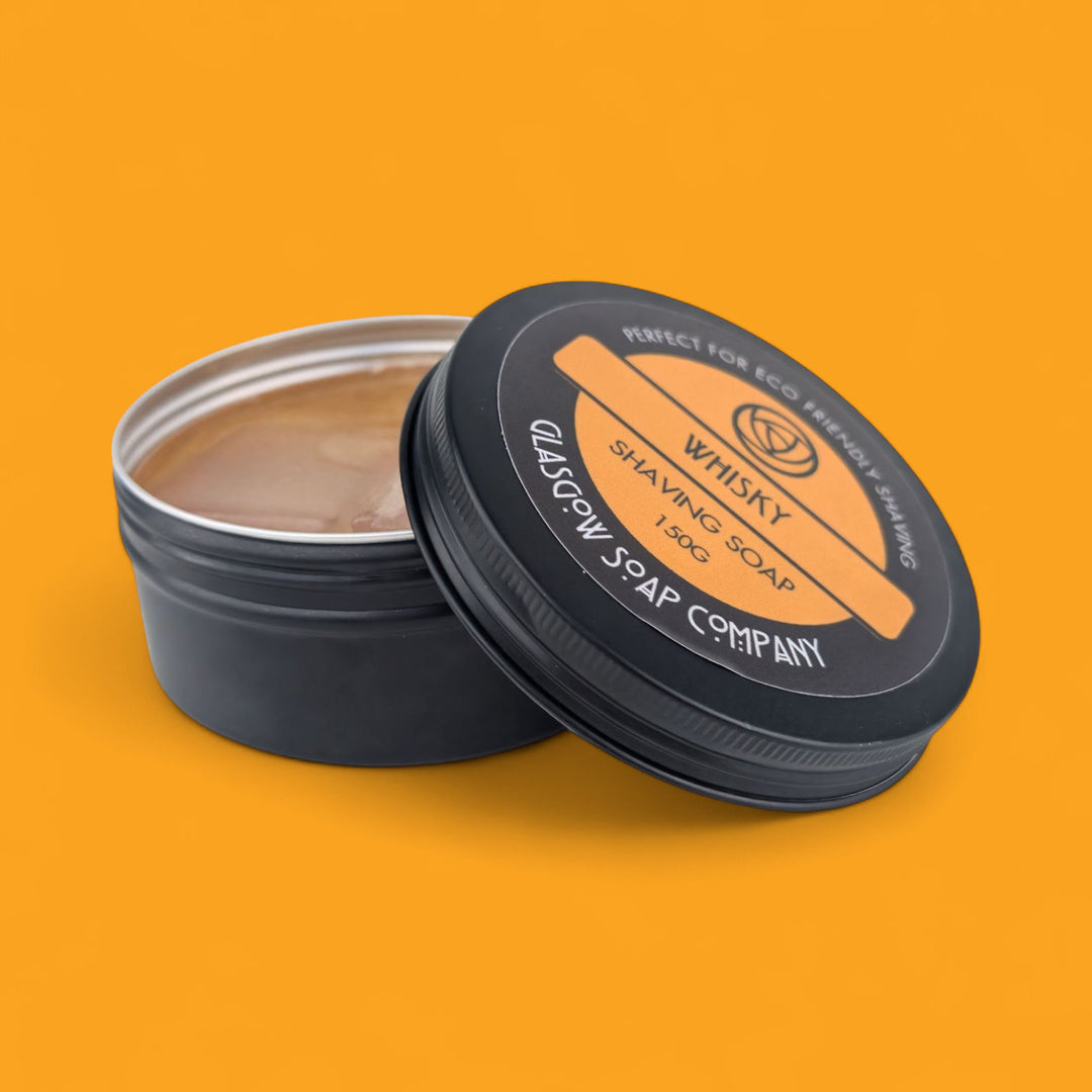 Black container of whisky shaving soap with visible branding on an orange background