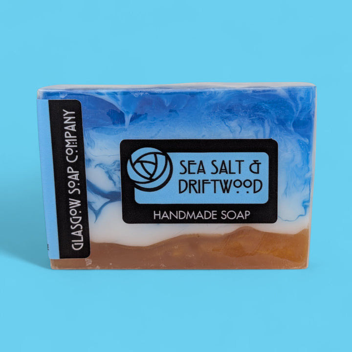 Handmade soap bar with 'Sea Salt & Driftwood' scent on a blue background