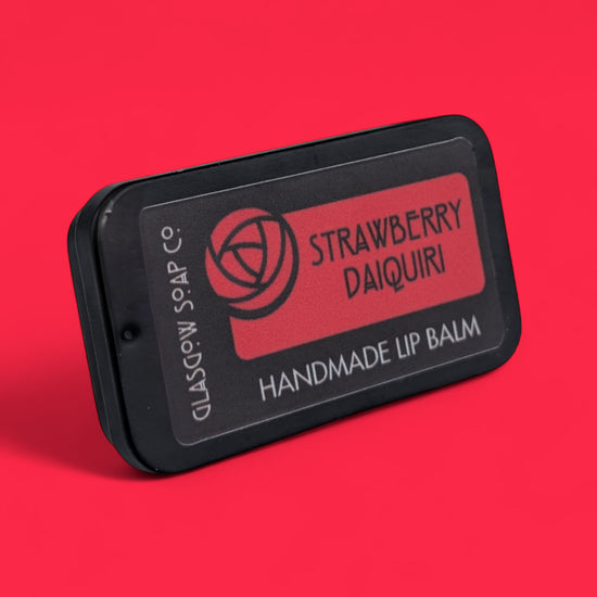 Handmade lip balm with 'Strawberry Daiquiri' flavor on a red background