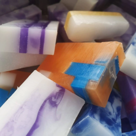 A variety of handmade soap slices with various colors and patterns, including white with purple swirls, orange with blue stripes, and blue with white edges.